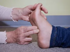Two hands gently holding a foot, gently flexing toes back and touching instep with two fingers.